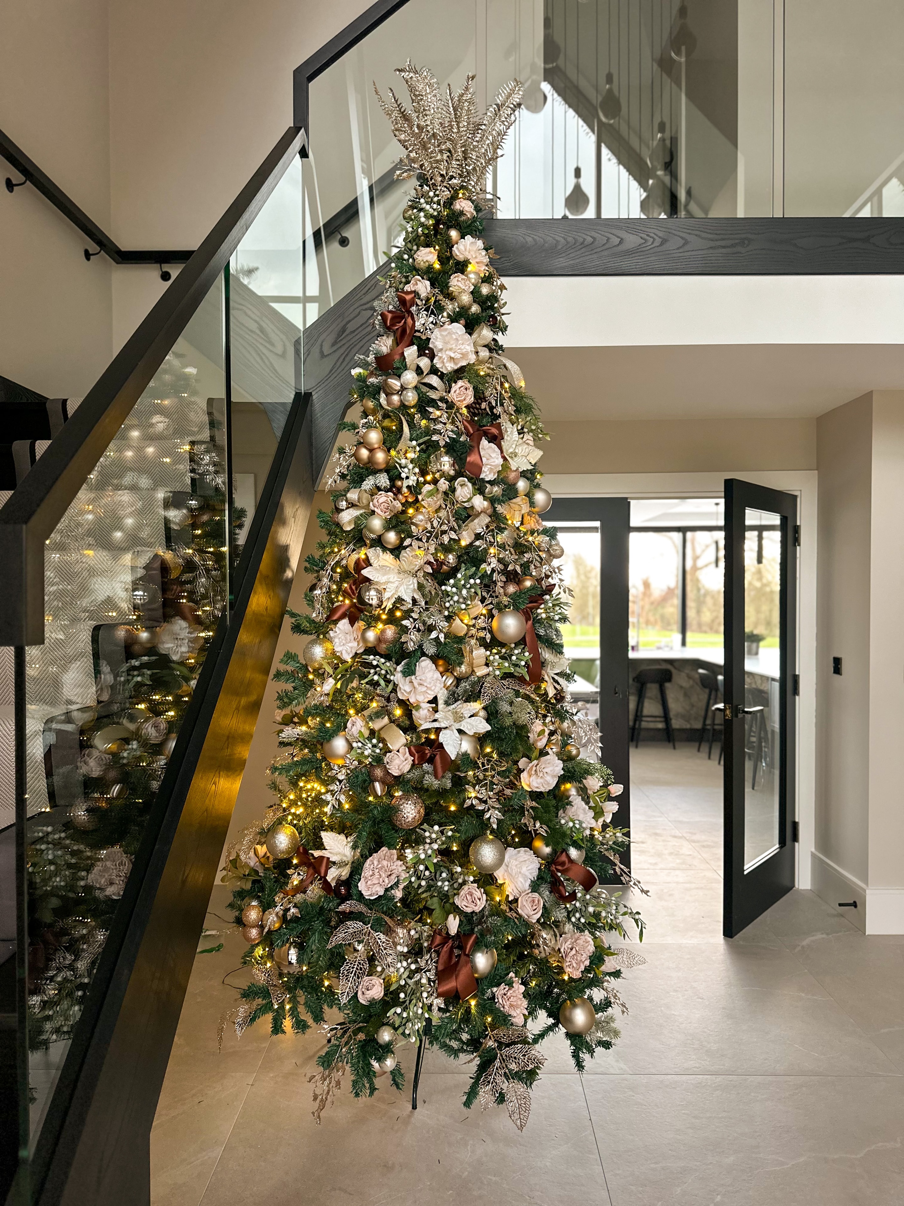 Luxury Christmas tree with blush florals and gold ornaments in modern hallway