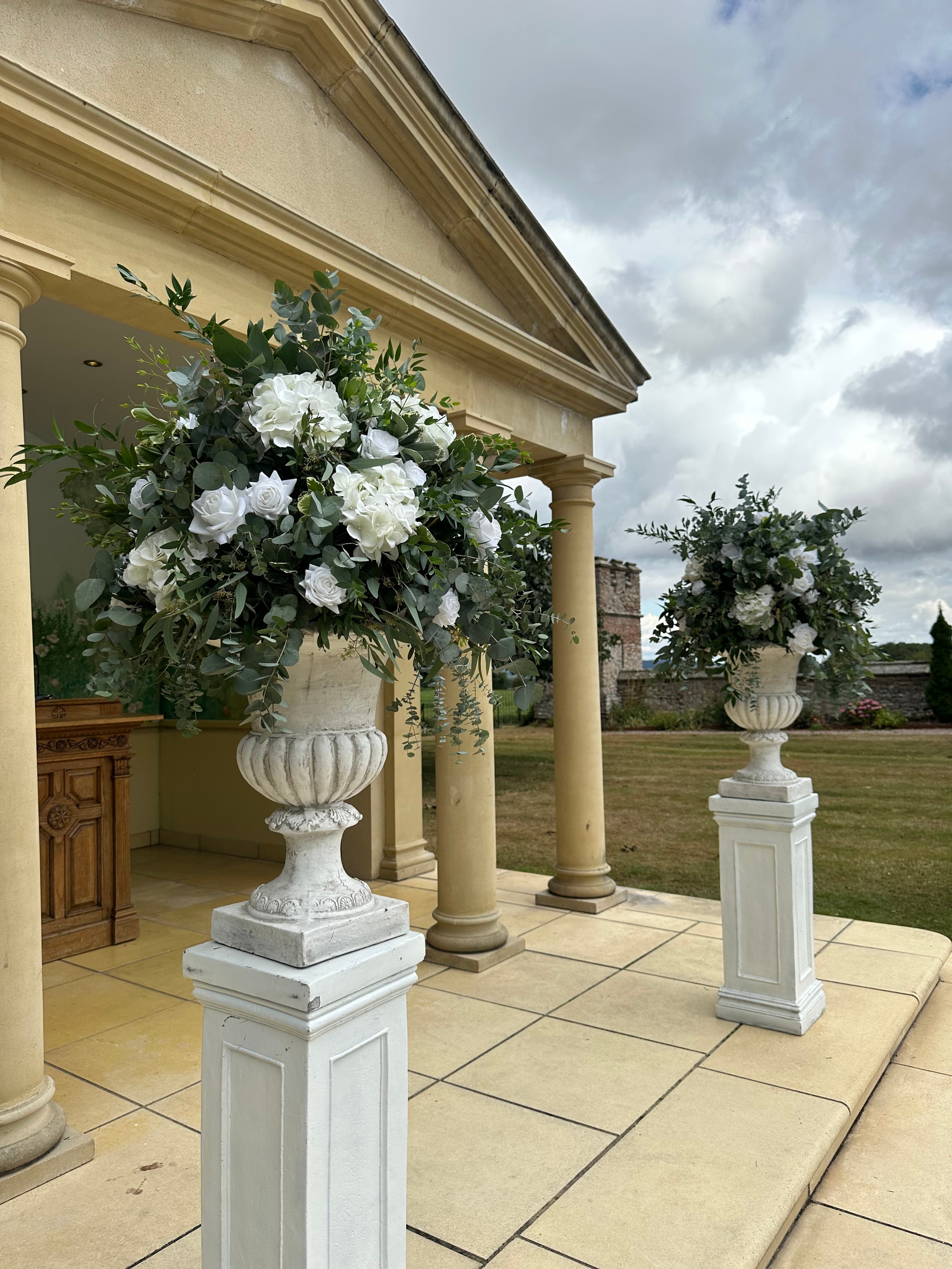 Stone urns with white roses and eucalyptus at grand country house entrance