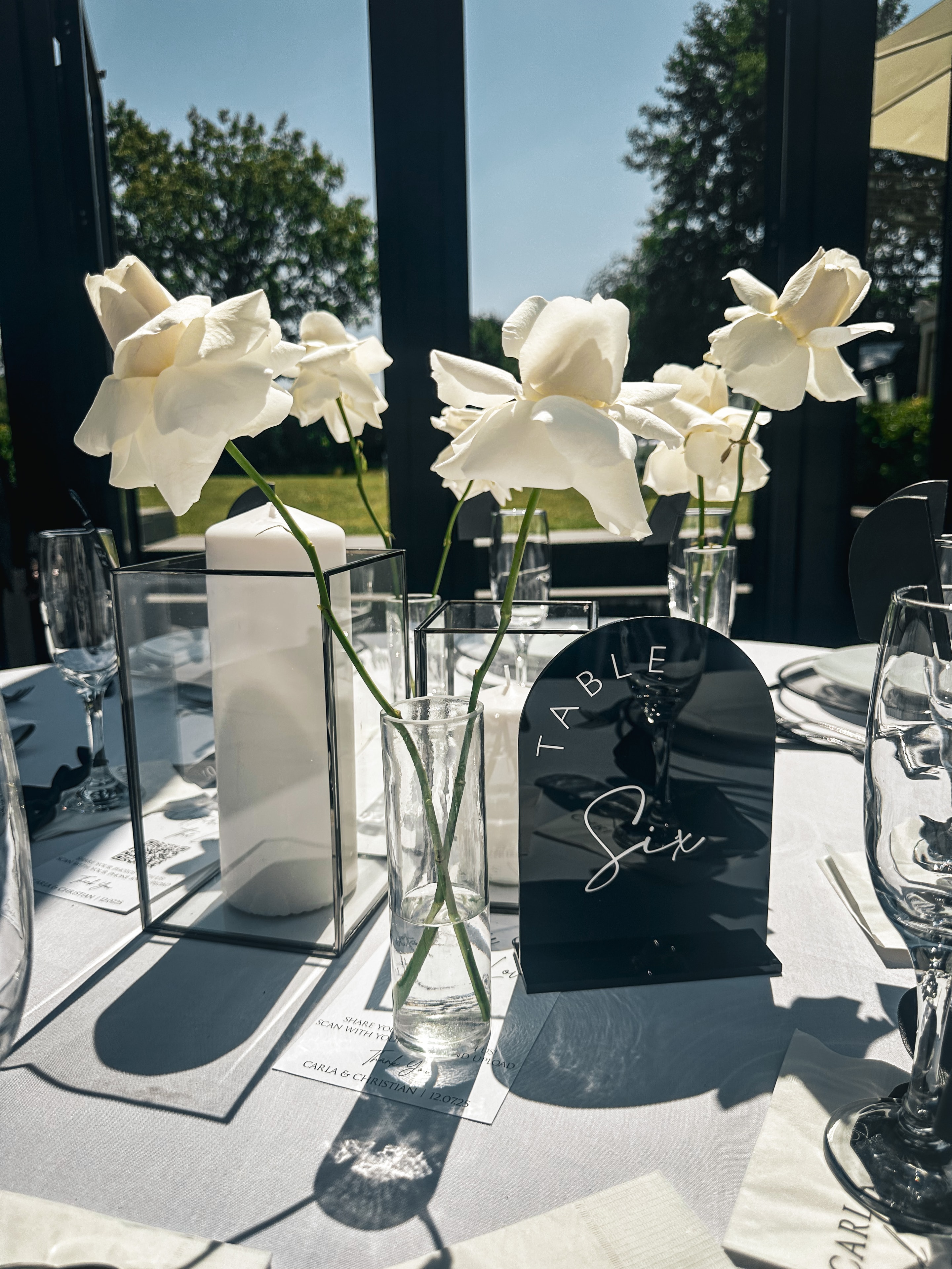 Modern outdoor table setting with white orchids black table number and glassware