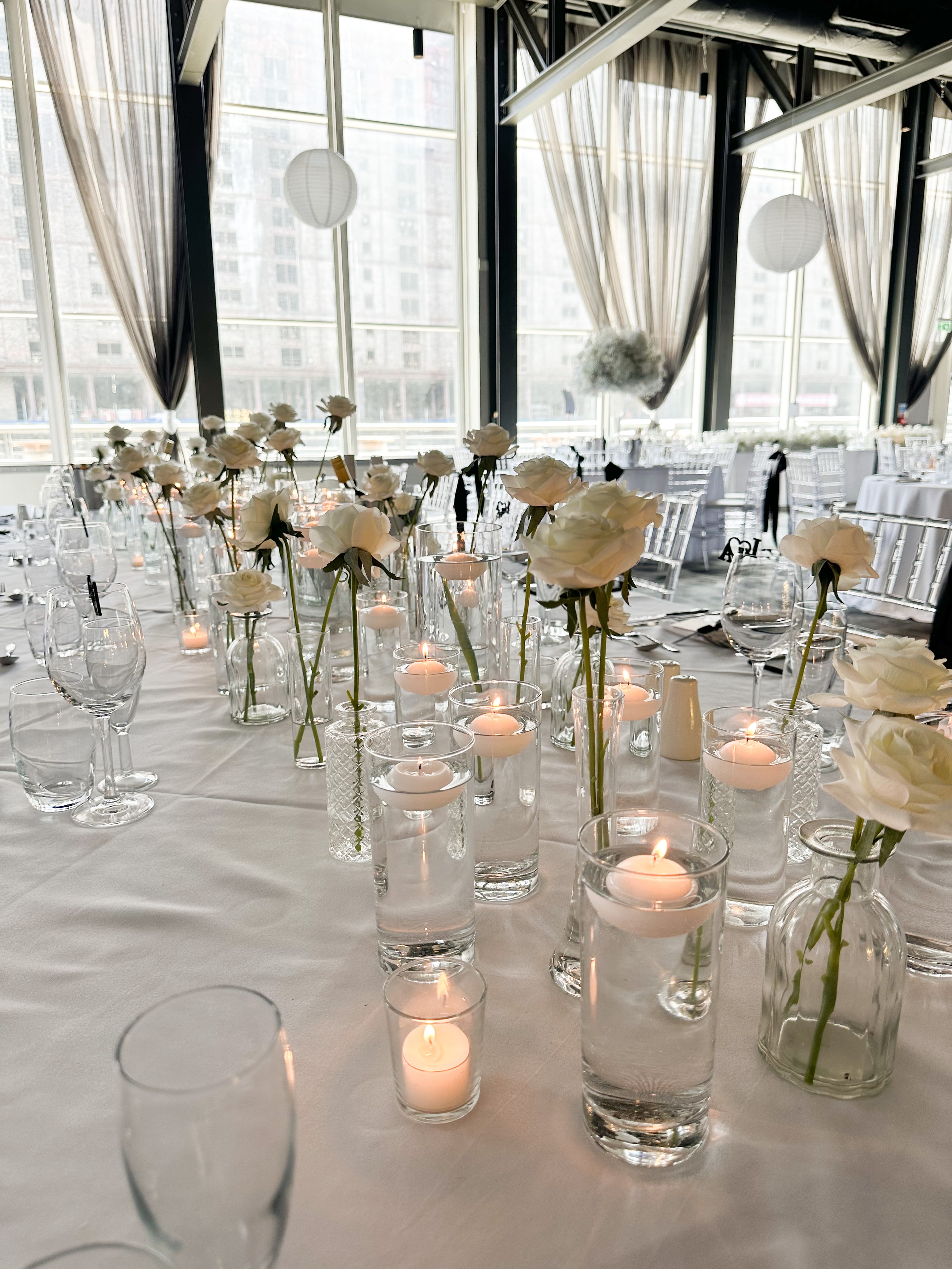 Modern venue reception tables with white roses bud vases and floating candles